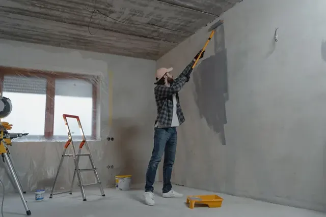 Peintre préparant et peignant le mur d’une pièce en rénovation